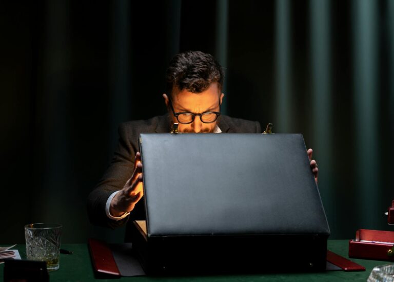 A man in a black suit is intriguingly opening a briefcase in a dimly lit room.