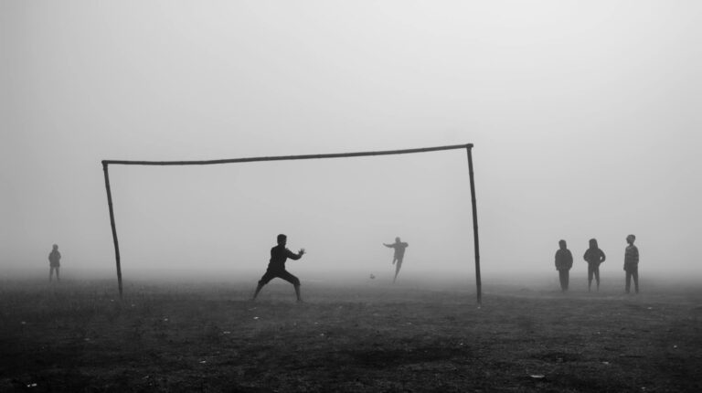 Dramatic black and white silhouette of children playing soccer in a foggy field.