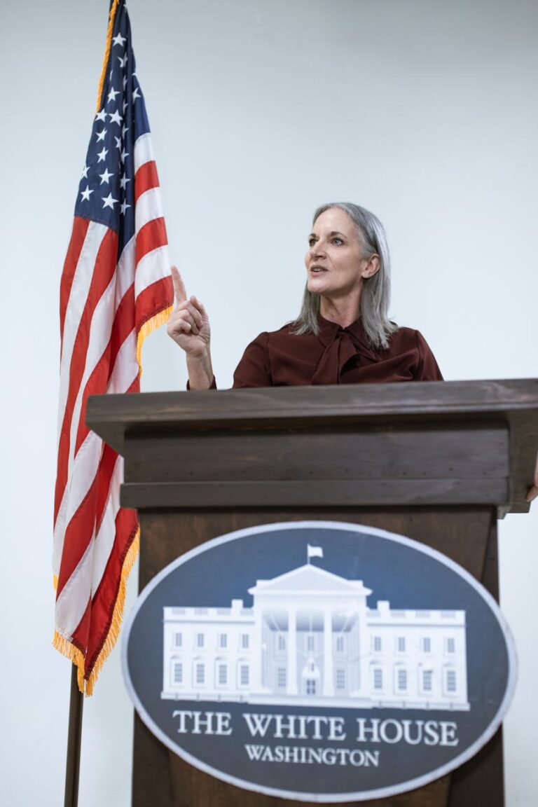 A woman speaking at a podium with the American flag, symbolizing leadership and patriotism.