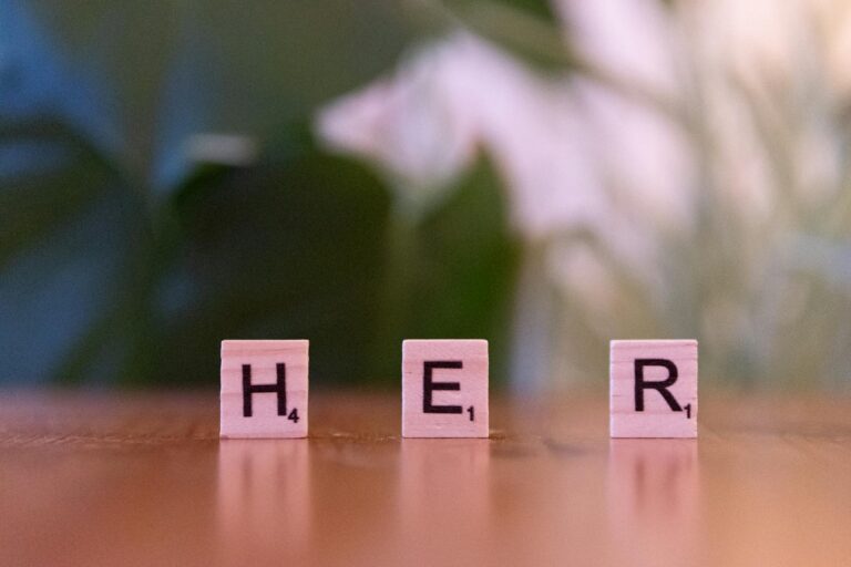 Scrabble tiles spelling the word 'HER' on a wooden surface, blurred background.