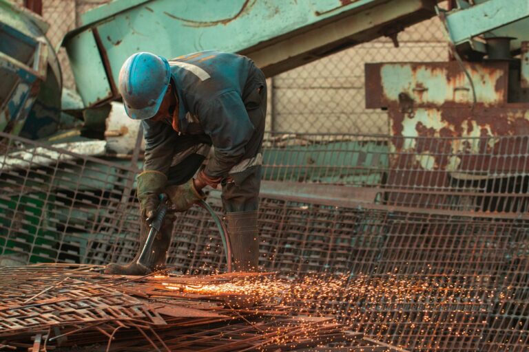 A skilled welder using a torch on scrap metal in an industrial setting, with sparks flying.