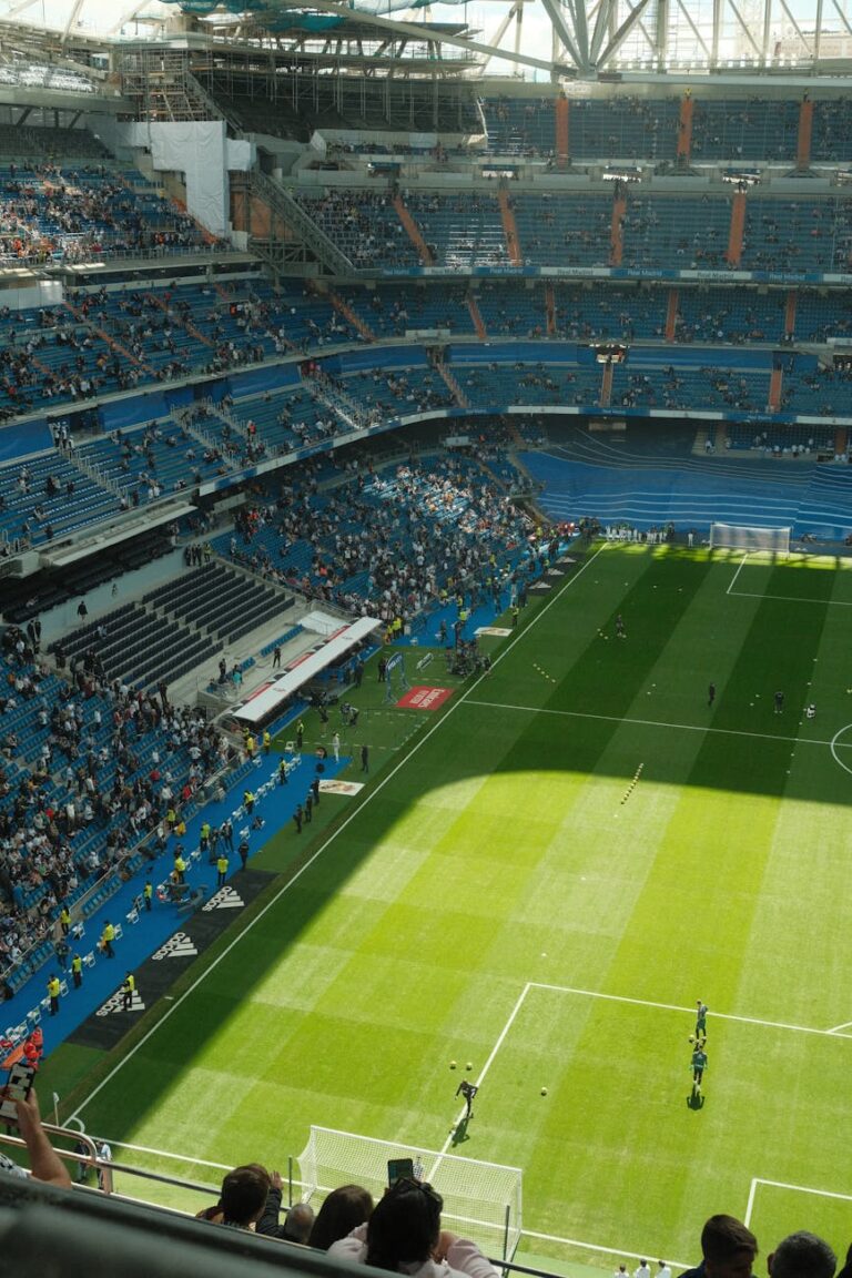 Aerial view of a sunlit soccer stadium with fans in the stands, capturing the vibrant atmosphere.