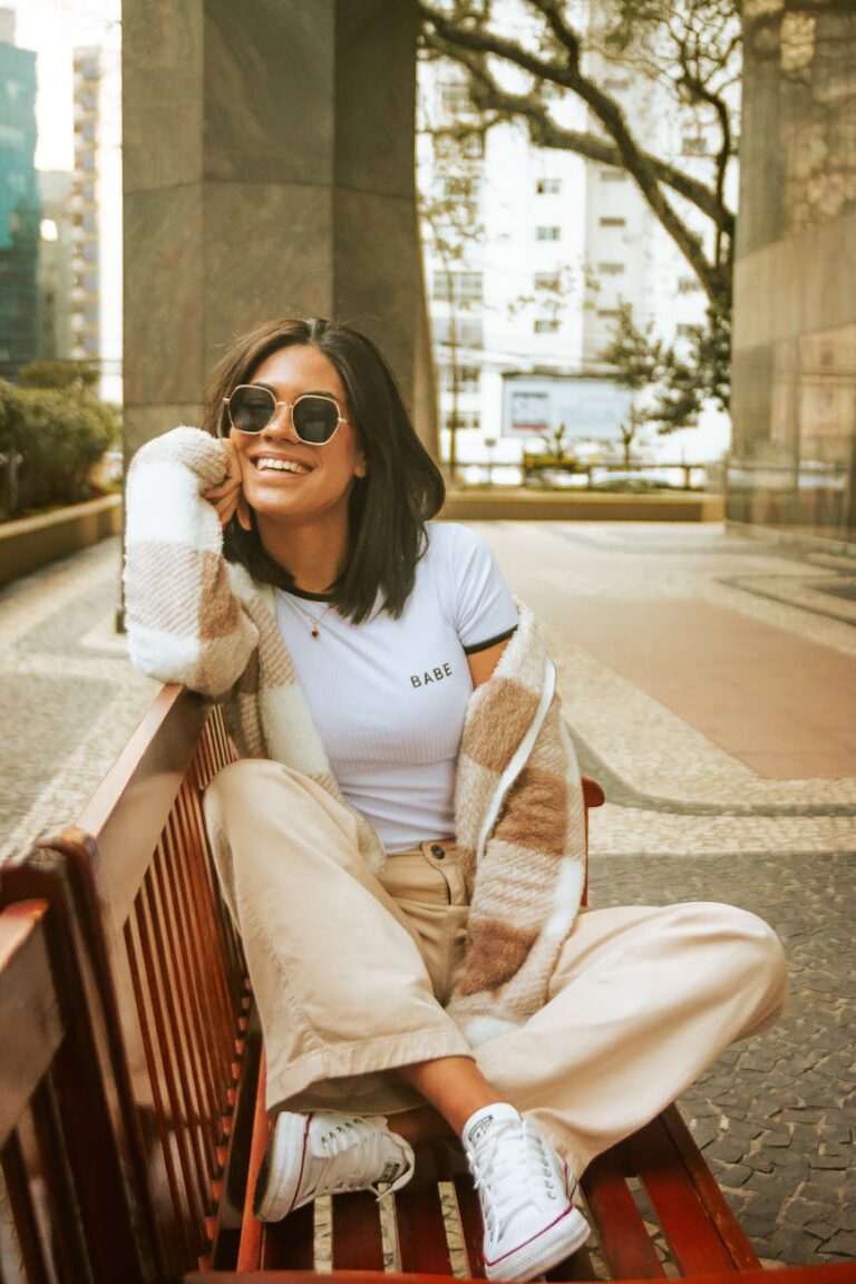 A fashionable woman with sunglasses smiling while sitting on a bench in São Paulo, Brazil.