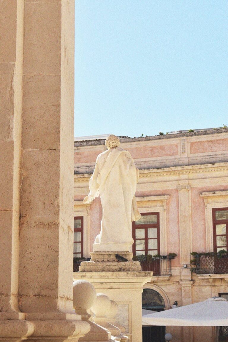 Marble statue in a sunlit European courtyard with historic architecture.