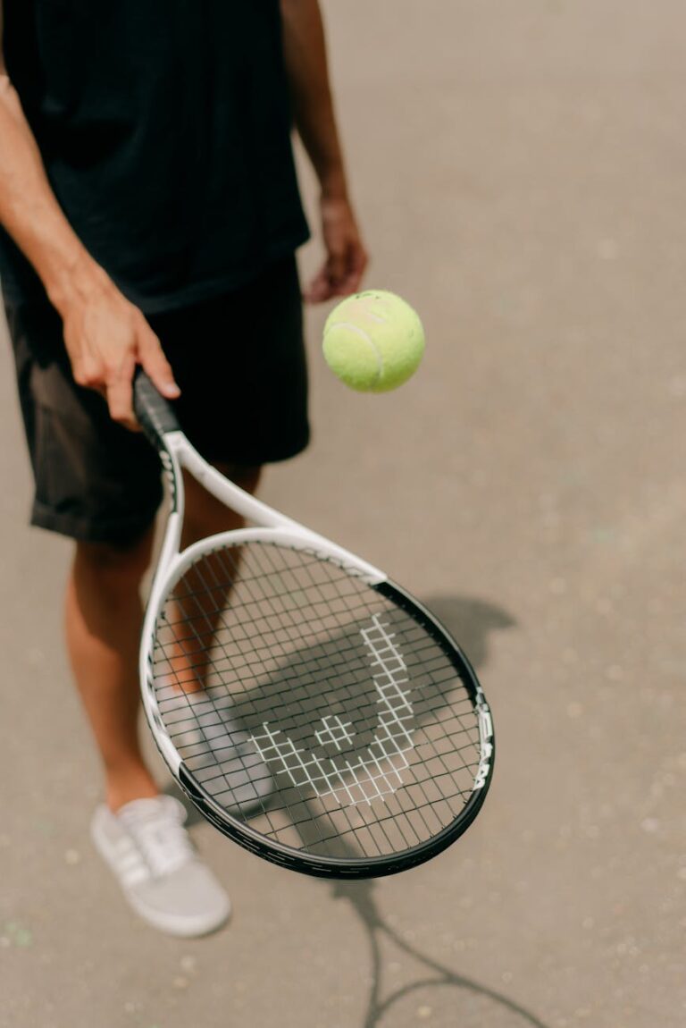 An adult tennis player holding a racket with a ball mid-air, captured outdoors.