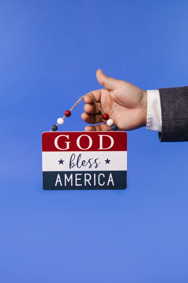 A hand holding a 'God Bless America' sign against a blue backdrop, symbolizing patriotism.