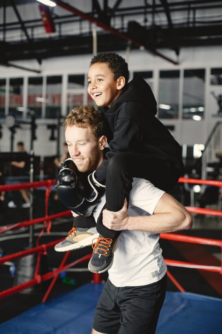 A father carries his son on his shoulders in a boxing gym, showcasing strength and joy.
