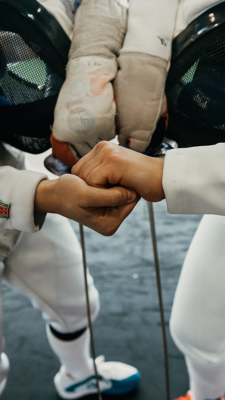 Close-up of two fencers shaking hands in full gear before a fencing match indoors.