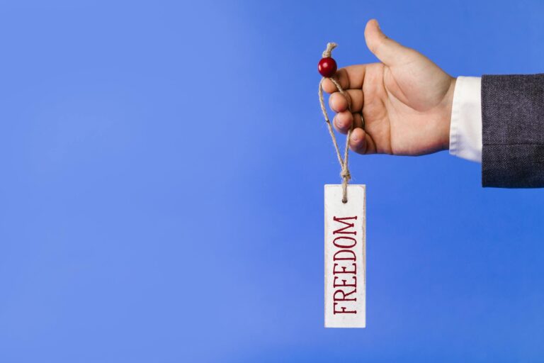 A businessman hand holding a freedom sign against a blue background, symbolizing liberty and motivation.