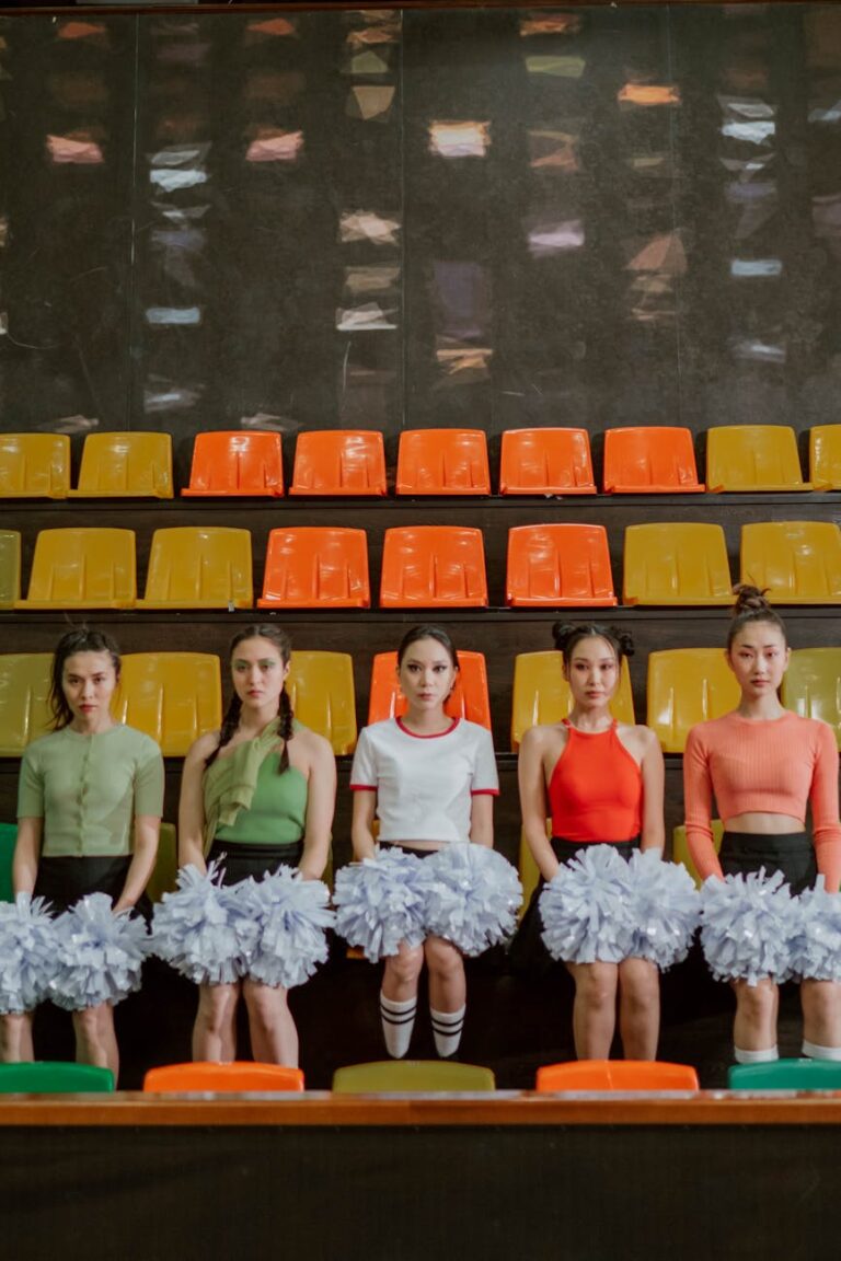 Cheerleading team with pompoms sitting in a vibrant, empty stadium.
