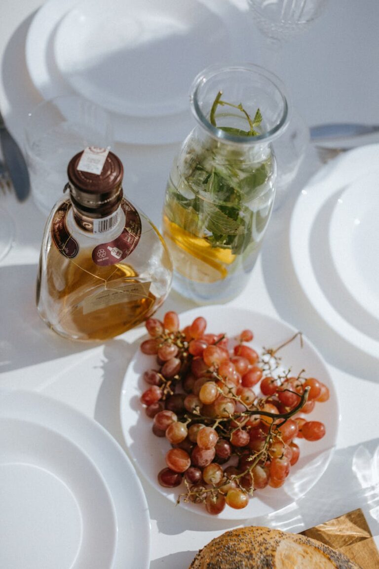 Beautiful table setting with grapes, a bottle, and infused water under sunlight.