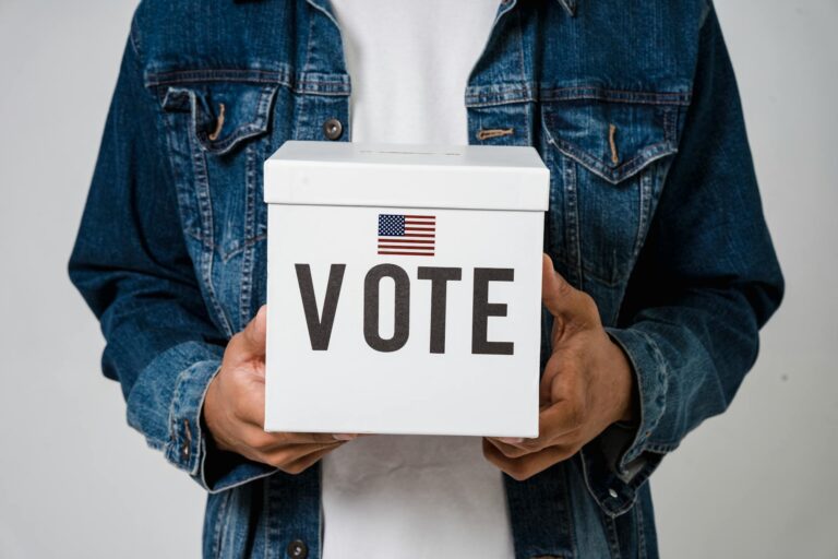 Person in denim holding a ballot box with a US flag, emphasizing voting rights.