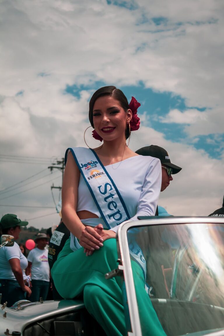 A pageant contestant smiles while sitting on a car in Mérida, showcasing vibrant urban culture.