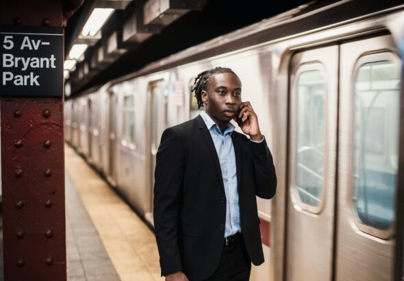 Serious African American male in formal suit talking on smartphone while waiting for underground train to stop