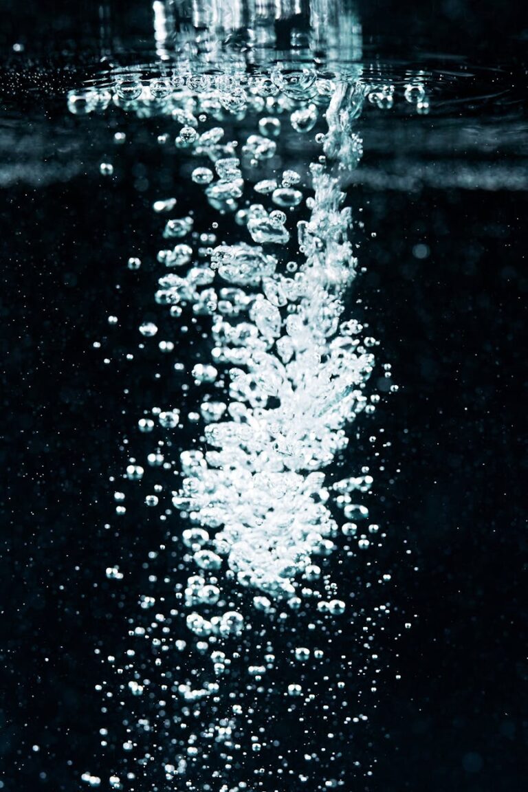 Macro shot of effervescent bubbles rising in water against a dark background.