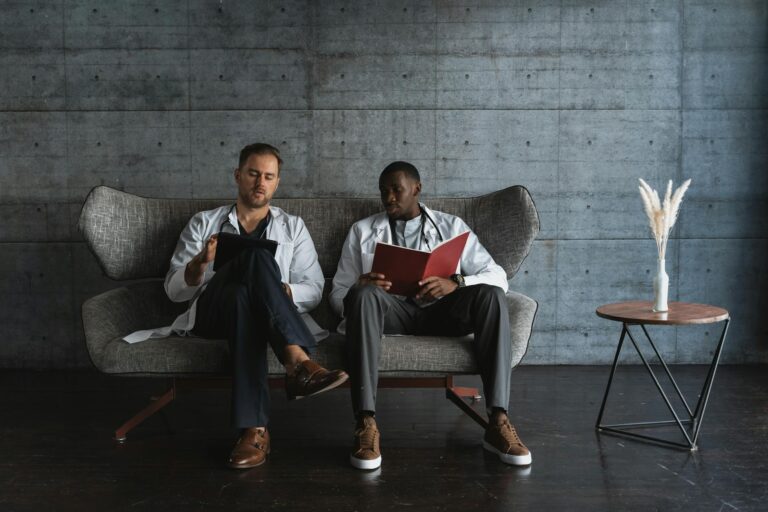 Two doctors in a modern office, reviewing patient files on a sofa.