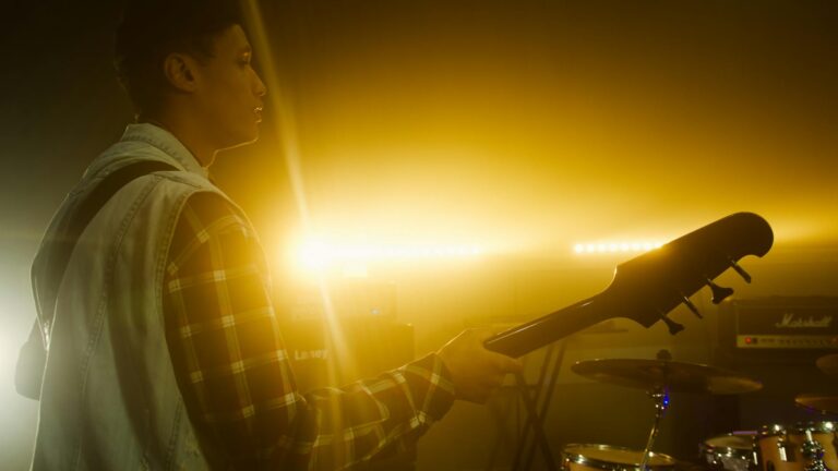 Silhouette of a guitarist playing on stage with dramatic backlighting during a sunset concert.