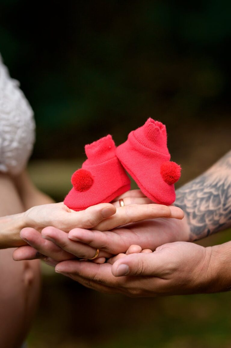 Close-up of expectant parents holding red baby shoes, symbolizing new life and family.