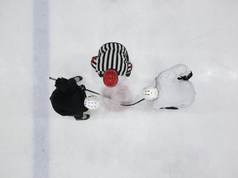 Top view of an ice hockey faceoff with players and referee on an ice rink.