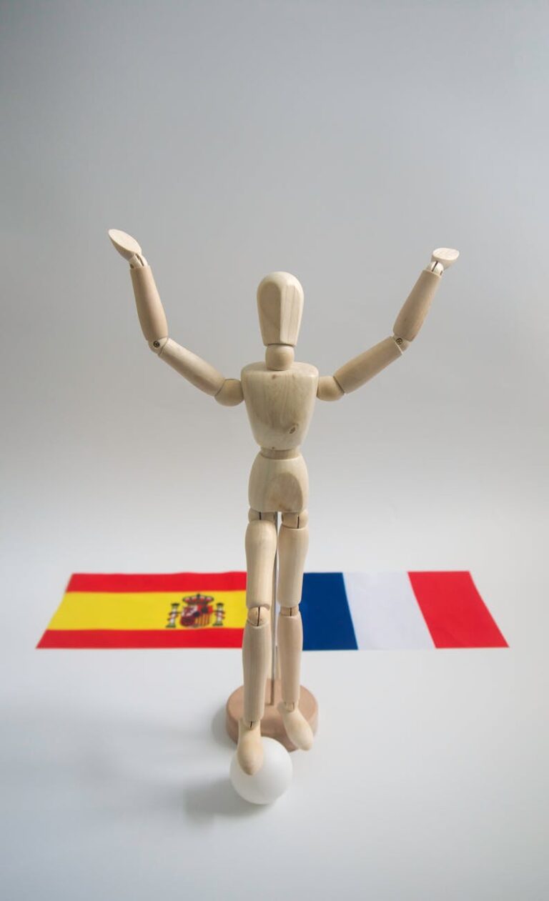 A wooden mannequin with raised arms stands before Spanish and French flags, symbolizing unity.