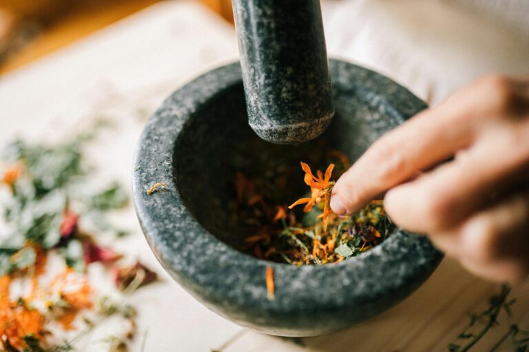 A hand crushes vibrant herbs in a stone mortar, blending natural ingredients.