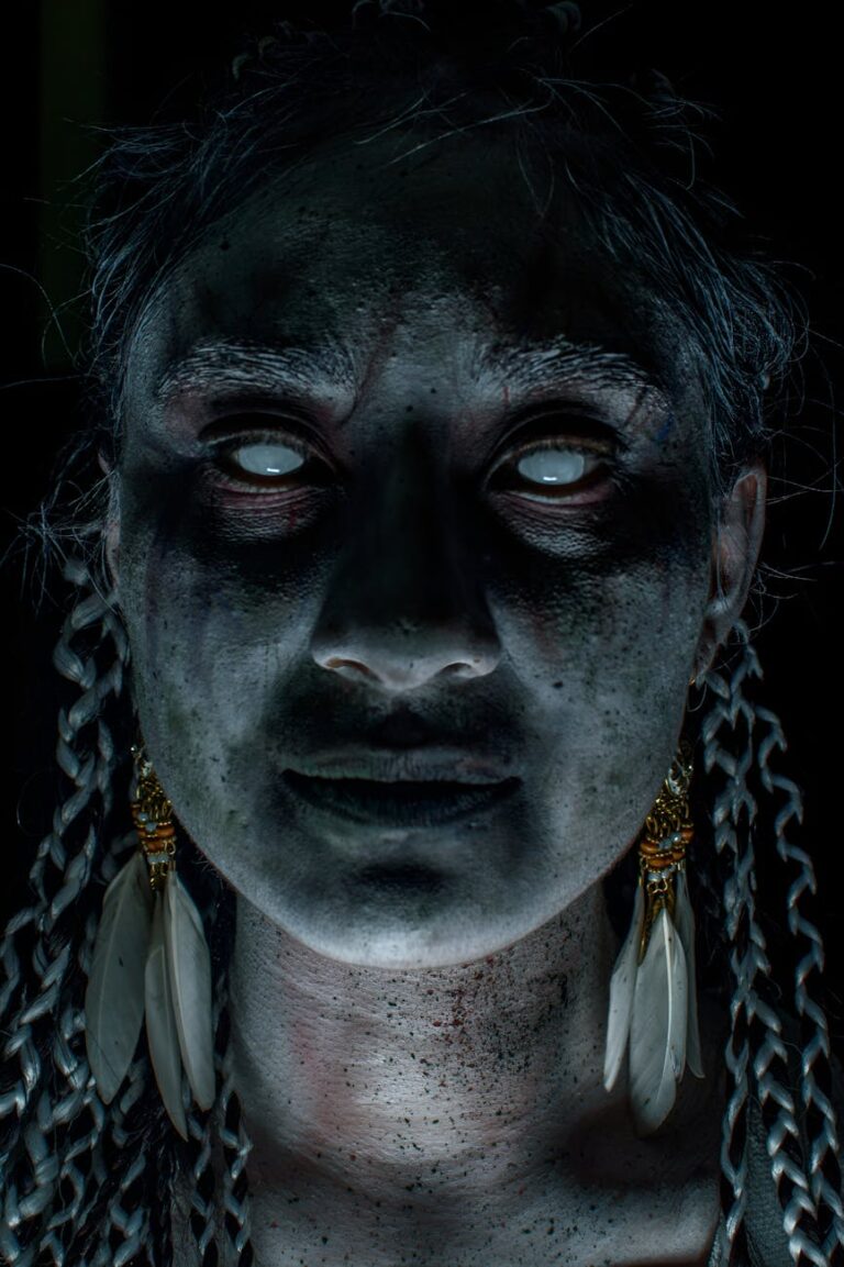 Haunting portrait of a woman with white eyes, braids, and feather earrings. Perfect for Halloween themes.