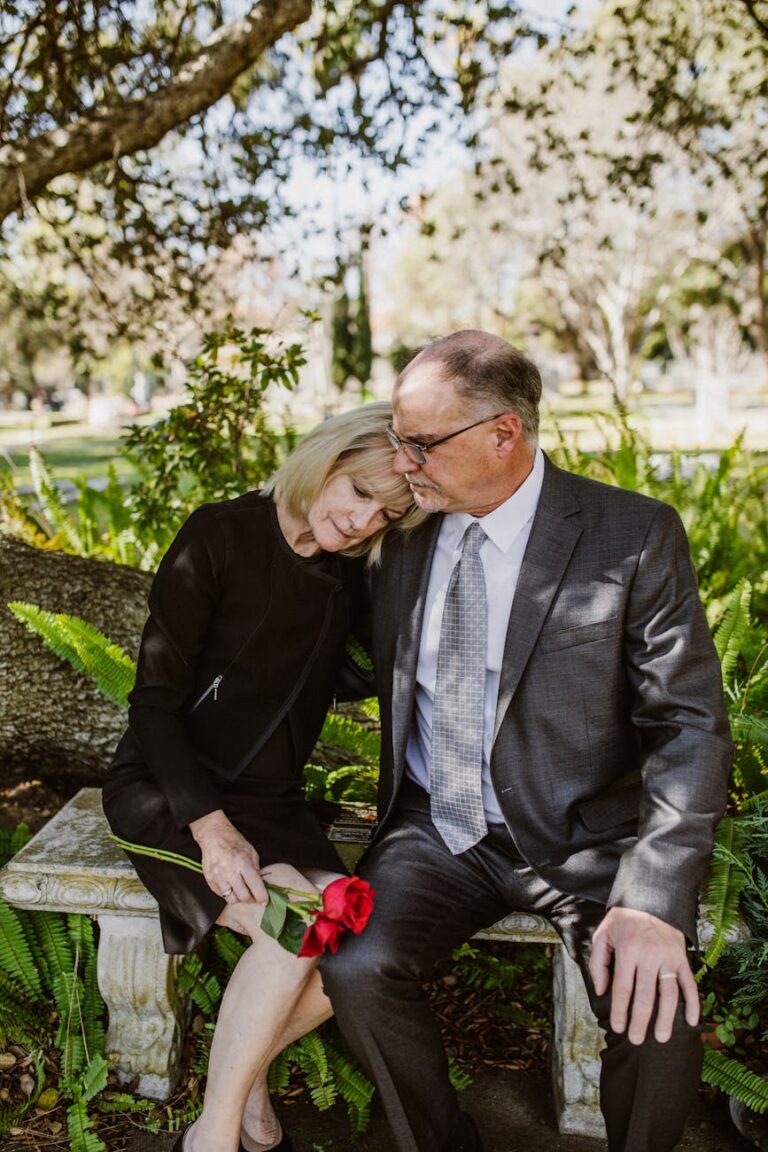 A grieving couple sitting on a bench in a sunny park, holding roses, expressing love and loss.