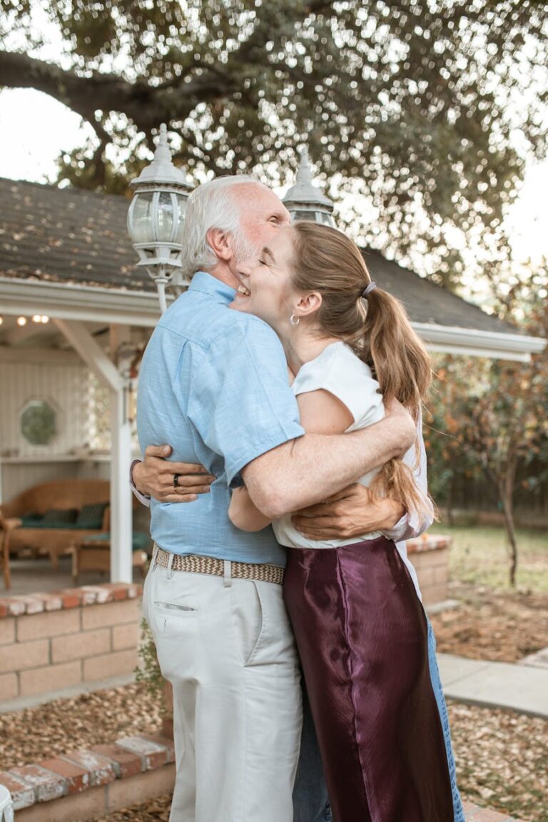 A touching moment between an elderly father and his adult daughter sharing an embrace in a garden.