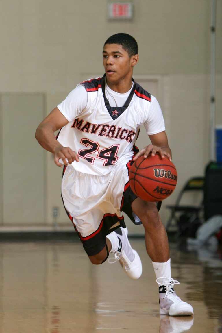 A young male basketball player dribbles on an indoor court wearing a Maverick jersey.