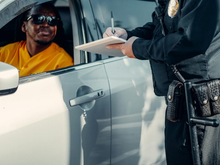 A police officer writes a ticket for a driver in a car during a roadside stop.