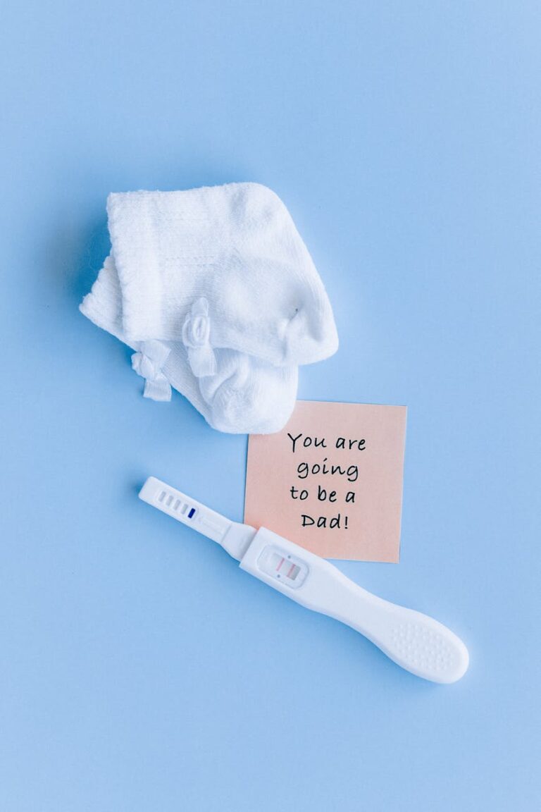 Pregnancy announcement items on blue background, including test, socks, and note.
