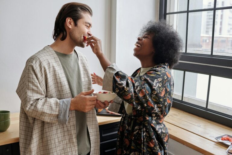 Happy couple sharing a joyful breakfast moment with laughter and fruit indoors.