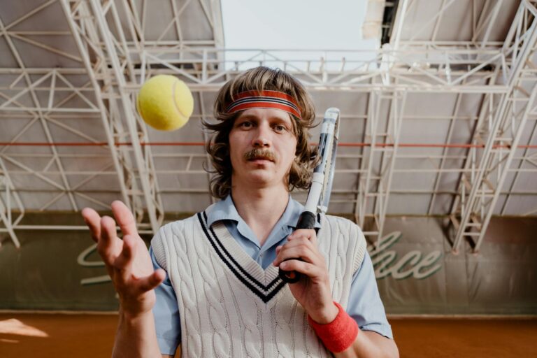 Vintage style tennis player with mustache and headband posing indoors with racket and ball.