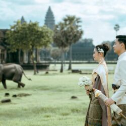 Elegant Cambodian couple in traditional attire at Angkor Wat with an elephant in the background.