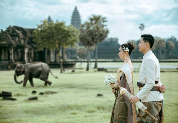 Elegant Cambodian couple in traditional attire at Angkor Wat with an elephant in the background.