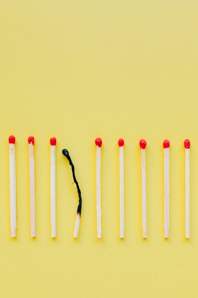 A line of matchsticks with one burned out symbolizes burnout and exhaustion against a yellow background.