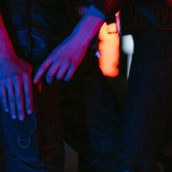 Close-up of a person in cyberpunk attire holding a futuristic weapon, illuminated by neon lights.