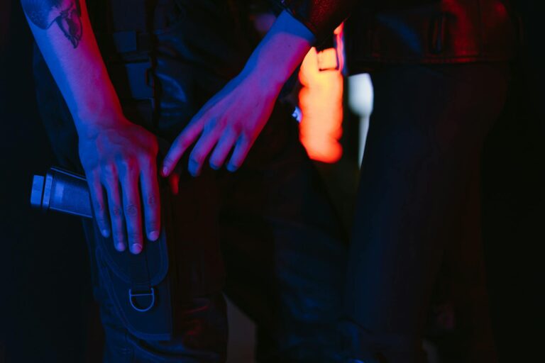 Close-up of a person in cyberpunk attire holding a futuristic weapon, illuminated by neon lights.