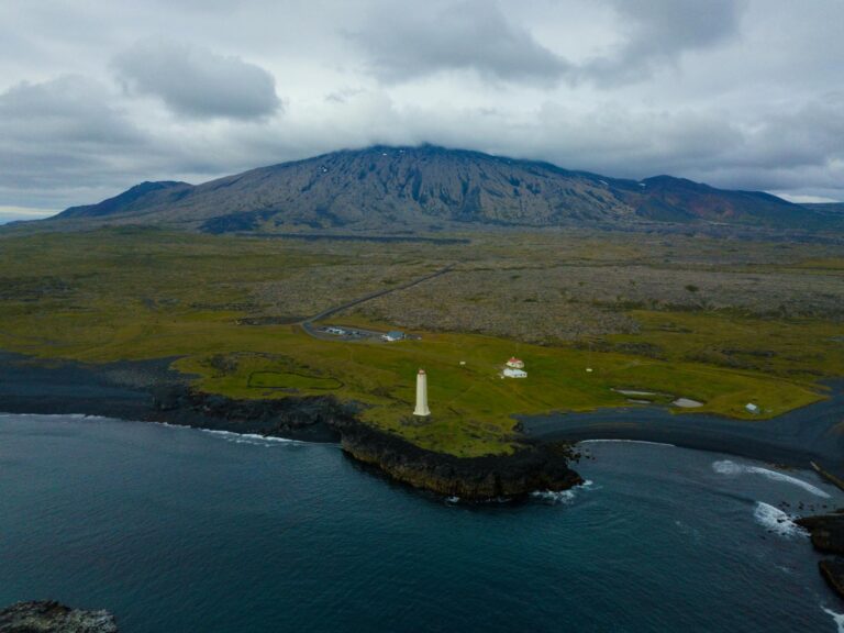 Breathtaking aerial shot of the Snæfellsnes Peninsula with a lighthouse, rocky coastline, and majestic mountains.