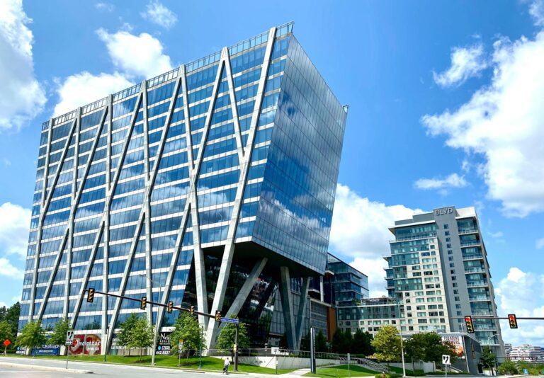 Tall modern office building with glass facade in an urban setting under a clear blue sky.