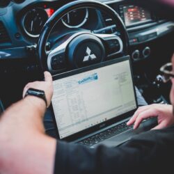 A person using a laptop inside a car for vehicle diagnostics, showcasing technology integration in automotive settings.