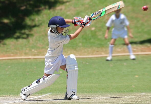 Young cricketer in white gear executing a sweep shot on a sunny day.