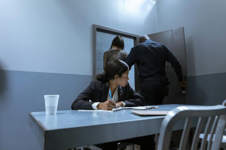 Police officer escorting suspect as lawyer observes during interrogation.