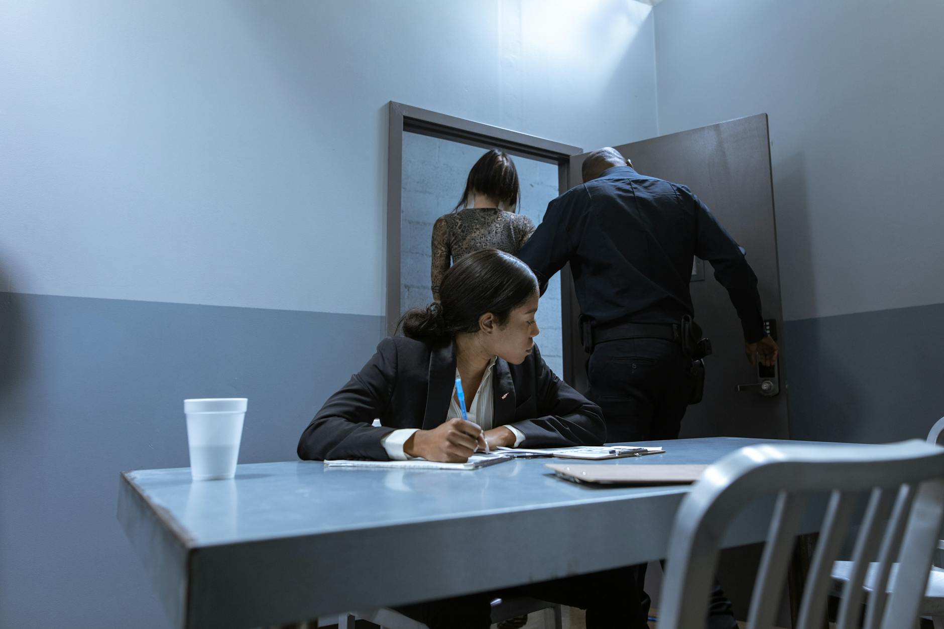 Police officer escorting suspect as lawyer observes during interrogation.