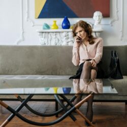 A woman sits thoughtfully on a sofa, engaged in a phone call in a stylish living room.