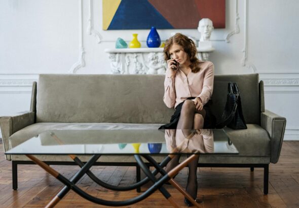 A woman sits thoughtfully on a sofa, engaged in a phone call in a stylish living room.