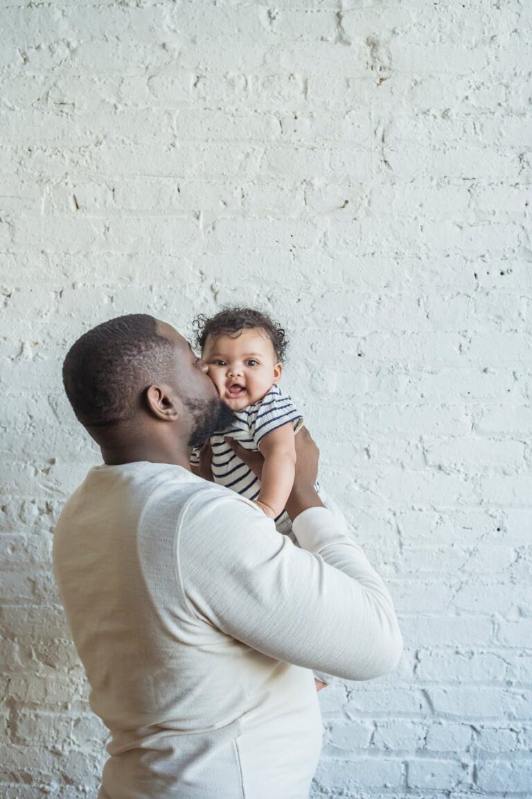 Affectionate father holding smiling baby against a rustic brick wall.