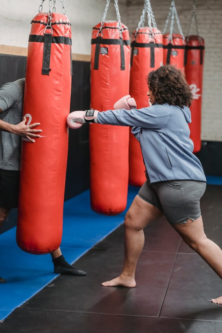 Active overweight African American female in boxing gloves hitting punching bag during workout in gym