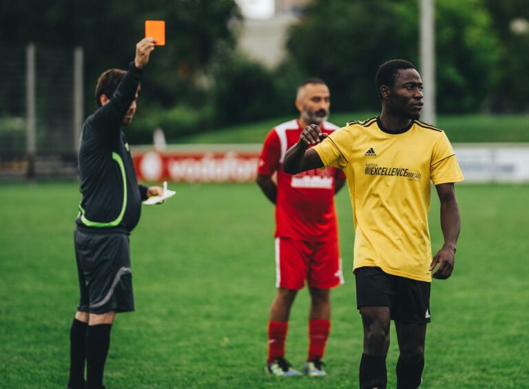 Referee issuing a red card to a soccer player in an outdoor match setting.