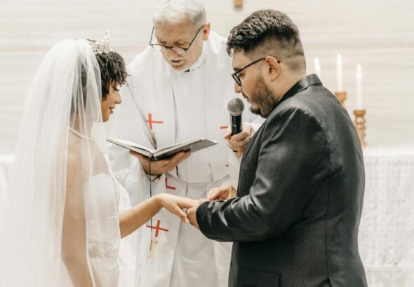 Bride and groom exchanging vows in a church ceremony led by a priest.